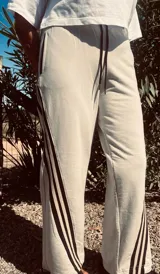 Pantalón deportivo color naranja con las icónicas tres rayas blancas laterales características de la marca Adidas.