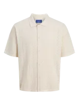 Polo loose de tejido estructurado color beige, con cuello tipo polo, mangas cortas, hombros caídos y cierre frontal con botones.