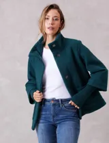 Tapado de tejido bouclé color marrón, con silueta evasé y largo a la cadera. Presenta cuello alto envolvente, cierre frontal oculto con botones a presión y bolsillos frontales de gran tamaño. Sus mangas son 3/4 con corte amplio y puños de tejido rib al tono que se extienden para cubrir las muñecas.