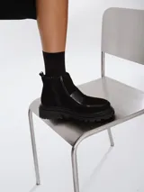 Botinetas negras de estilo urbano con suela track, confeccionadas en una combinación de gamuza y cuero sintético. Presentan cierre lateral y un diseño de puntera reforzada.