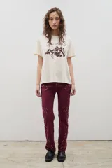 Pantalón de denim negro con diseño de tachas metálicas distribuidas en patrones curvos. Presenta un corte recto y tiro medio.