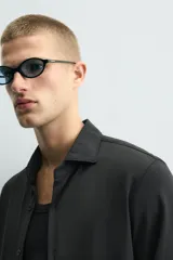 Camisa de manga larga color verde oscuro, con cuello italiano abierto y cierre frontal de botonadura. Presenta un calce ajustado (slim fit) y puños con botón.