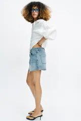 Falda pantalón de denim azul con diseño de cinco bolsillos, cierre frontal con cremallera y botón, y bajo deshilachado sin costuras.