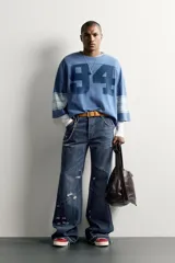 Camiseta boxy fit de color azul con efecto lavado vintage, cuello redondo y mangas por debajo del codo. Presenta un gran número '94' estampado en el frente y franjas horizontales en las mangas.