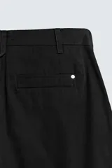 Pantalón chino de corte wide fit confeccionado en tejido de algodón. Presenta pliegues frontales, bolsillos laterales y bolsillos traseros de vivo, con cierre frontal de cremallera y botón.