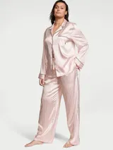 Pijama largo de satín con estampado de rayas verticales en tonos rosados y blancos, compuesto por una camisa de manga larga con botones y ribetes negros, y un pantalón largo a juego.
