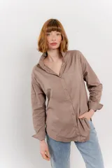 Camisa color marrón claro, de corte clásico y holgado, con cuello camisero, cierre frontal con botones, bolsillo en el pecho y mangas largas con puños abotonados.