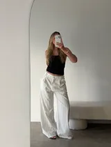 Pantalon de corte sastrero y pierna ancha, confeccionado en tela de algodón color blanco con estampado de rayas verticales finas en color negro. Presenta pinzas en la cintura, cierre frontal con botón y bolsillos laterales.