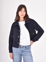 Chaqueta corta de paño en color azul oscuro, con cuello camisero, cierre frontal con botones metálicos dorados y dos bolsillos frontales con solapa.