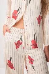 Pijama de satén compuesto por una camisa de manga larga con botones y un pantalón largo, ambos de color crudo con estampado de rayas verticales negras y flores rojas.
