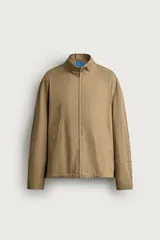 Cazadora regular fit de la colección Aaron Levine x ZARA, confeccionada en tejido con mezcla de algodón con patrón de cuadros pequeños en tonos beige y marrón. Cuenta con cuello subido, manga larga con puño ajustable con botón a presión, bolsillos de vivo en la cadera, bajo ajustable con elástico en los laterales y cierre frontal con cremallera.