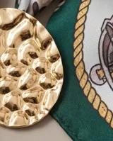 Pañuelo de seda estampado con diseño de cadenas, lunares y detalles geométricos en tonos verde, marrón, blanco y dorado. Incluye un dije ovalado dorado con textura martillada.