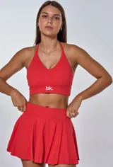 Conjunto deportivo compuesto por un top con escote en V y espalda deportiva, y una pollera short con diseño plisado. El top presenta el logo de la marca estampado en el frente.