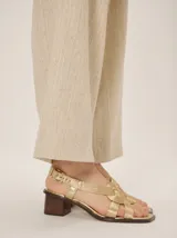 Sandalias de cuero metalizado color bronce, de taco bajo, punta cuadrada y tiras cruzadas en el empeine con textura acanalada. Posee tira al tobillo ajustable con hebilla metálica dorada.