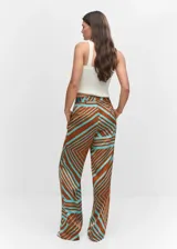 Pantalón de tiro medio con diseño recto y fluido, confeccionado en tejido satinado con estampado geométrico en tonos marrón y turquesa. Cuenta con cierre oculto de botón, gancho y cremallera, trabillas para cinturón, pinzas delanteras y dos bolsillos laterales.