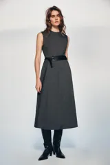 Vestido midi de cuello redondo y sin mangas, confeccionado en tejido jaspeado gris. Presenta un corte evasé y un cinturón ancho de cuero sintético negro con hebilla metálica. Incluye cierre posterior con cremallera oculta.