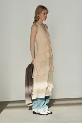 Vestido midi de escote en pico con lazada frontal y diseño sin mangas. Presenta múltiples niveles de volantes a lo largo de la falda y cierre lateral con cremallera oculta.