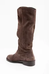Bota de caña alta confeccionada en gamuza color marrón, con diseño de caña holgada y suela plana con pequeño taco cuadrado.