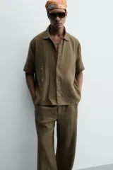 Camisa de corte relajado confeccionada en lino color verde militar, con cuello solapa, manga corta y cierre frontal de botones.