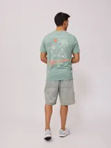 Remera negra de algodón con estampado en la espalda con palmeras, tabla de surf y texto en color blanco y fucsia.