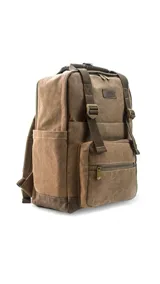 Mochila urbana de tela canvas color marrón, con diseño funcional que incluye compartimento para notebook de 15 pulgadas y espacio interior organizado para set de mate. Cuenta con correas ajustables, manija superior reforzada, bolsillo frontal con cierre y detalles en cuero sintético.
