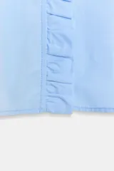 Camisa de color celeste con cuello subido, manga larga abullonada con puños elásticos y detalle de volantes en el cuello y a lo largo de la botonadura frontal.
