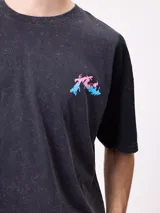 Remera de algodón con calce oversize, color negro con efecto lavado. Presenta un estampado gráfico en la espalda con diseño de espiral en tonos rosado y celeste, acompañado de inscripciones decorativas.