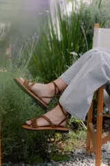 Sandalias bajas de cuero color marrón, con tiras finas para atar alrededor del tobillo.