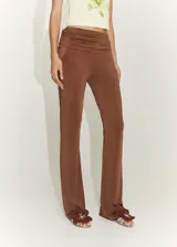 Pantalon de tiro bajo color marrón, con diseño acampanado y detalle drapeado en la cintura. Confeccionado en tejido fluido de punto circular.