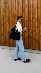 Cartera tipo tote de símil gamuza color negro, con diseño amplio y detalle de tachas metálicas en las costuras y las asas de hombro.