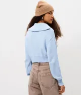 Campera cropped de tricot color blanco off-white, confeccionada en algodón con textura acanalada. Presenta cuello amplio con cierre metálico frontal, mangas largas con puños acanalados y cintura marcada con banda ancha.