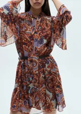 Vestido corto con estampado paisley en tonos marrón, naranja, celeste y lila. Tiene cuello redondo con lazo, mangas largas acampanadas, forro interior y cinturón desmontable.