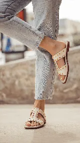Sandalias planas de cuero negro, con diseño de tiras anchas interconectadas y punta cuadrada, decoradas con tachas metálicas doradas.