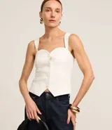 Blusa de sastrería color blanco, sin mangas, con escote corazón, breteles anchos y cierre frontal con botones forrados. Presenta un dobladillo en punta y espalda elástica.