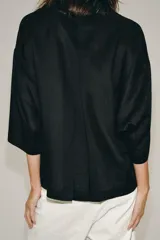 Camisa amplia confeccionada en hilatura con lyocell y ramio, color celeste, con cuello solapa, manga por debajo del codo, detalle de pliegue en la espalda y cierre frontal con botones ocultos por solapa.