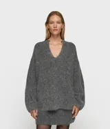 Sweater de punto oversize color gris, confeccionado en una mezcla de lana de alpaca con textura suave y peluda. Presenta cuello en V, mangas largas con hombros caídos y ribetes de canalé. Incluye una etiqueta decorativa en el puño de la manga izquierda.