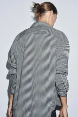 Camisa de corte fluido confeccionada en mezcla de viscosa, con diseño de rayas verticales en blanco y negro. Presenta cuello solapa, manga larga con puños, bolsillo de plastrón en el pecho, bajo redondeado y cierre frontal con botones.