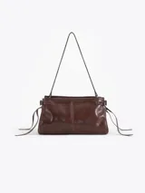 Bandolera de cuero vacuno color marrón con acabado brillante. Presenta un diseño estructurado con herraje metálico tipo candado y llave colgante en el frente, además de detalles de tiras laterales. Incluye correa de hombro y cierre superior.