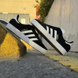 Championes adidas Gazelle ADV de corte bajo, confeccionados en gamuza negra con las icónicas tres tiras laterales en blanco. Presentan suela de goma blanca, lengüeta blanca con logo y detalle de marca Gazelle en dorado en el lateral.
