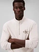 Buzo Calvin Klein de felpa de algodón color blanco off-white, con cuello alto, cierre de media cremallera y manga larga con puños acanalados. Cuenta con el logo de la marca bordado en el pecho.