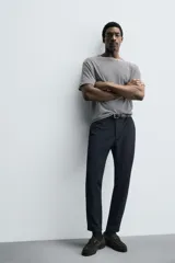 Pantalón de corte slim fit y color negro, confeccionado en tejido elástico. Cuenta con cintura elástica, trabillas, bolsillos frontales y cierre con cremallera y botón.