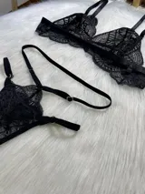 Conjunto de lencería de cuatro piezas en encaje negro, compuesto por bralette, tanga con tiras regulables, portaligas y ligas para piernas.