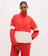 Campera deportiva de cuello alto con diseño color blocking en rojo y blanco. Presenta cierre frontal parcial, mangas largas con puños elásticos y bordado decorativo en el pecho. Confeccionada en poliamida con tecnología dry para mayor transpirabilidad.