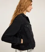 Campera de jeans de corte boxy, color azul medio lavado, con cuello, cierre frontal de botones, bolsillos con solapa y botones en el pecho, y recortes visibles.