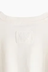 Remera de algodón color crema, corte oversized con hombros caídos y cuello redondo. Presenta un estampado frontal en negro de un pájaro (golondrina) sobre una cinta con el texto "COME UNDONE" y "Wuthering Heights".