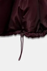 Campera puffer acolchada de color negro, con cuello envolvente, capucha integrada, manga larga, bolsillos laterales ocultos y bajo con elástico. Cierre frontal con botones a presión ocultos por solapa.