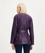 Campera alargada marca Cortelle confeccionada en poliuretano con textura que imita el cuero. Presenta cuello redondo, cierre frontal con botones metálicos, cuatro bolsillos delanteros con solapa y botones, y un lazo ajustable en la cintura.