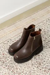 Botas cortas negras con plataforma dentada, confeccionadas en una combinación de cuero con textura de reptil y paneles de gamuza. Presentan un cierre frontal metálico y puntera cuadrada.