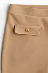Pantalón acampanado de punto roma en color tostado, con cintura elástica oculta y solapas de bolsillo decorativas con botones dorados en la parte frontal.