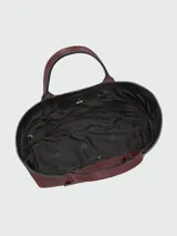 Bolso de hombro tipo tote bag de cuero color borgoña, con asas superiores y correa ajustable. Presenta un diseño estructurado con pliegues verticales y un detalle de borla colgante.